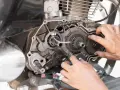 Mani che lavorano sul cambio di una moto, forse per risolvere una perdita di potenza auto benzina. Ingranaggi e meccanismi a vista.