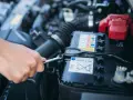 Mano con chiave inglese che lavora sulla batteria dell'auto. La batteria si scarica a vettura ferma, un problema comune per le auto con sistema Start & Stop.