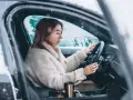 Donna al volante in un'auto coperta di neve, con le mani sul volante. Impara come guidare sulla neve in sicurezza.