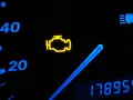 Cruscotto auto con spia motore accesa, indicatore di velocità e chilometraggio.