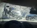 Vetro dell'auto coperto di brina, con segni di tergicristallo. Un sole pallido filtra attraverso il ghiaccio, rendendo difficile vedere. Ecco come sbrinare il vetro della macchina.