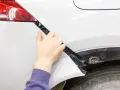 Mano che lavora alla riparazione paraurti in plastica di un'auto bianca.