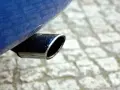 Il tubo di scarico cromato di un'auto blu, parte del silenziatore che attutisce il rumore del motore, su un selciato.