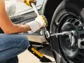 Persona con guanti gialli usa una chiave per serrare i bulloni della ruota di un'auto sollevata da un cric. Il significato di "nm" è la coppia di serraggio.