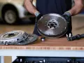 Meccanico mostra un volano auto nuovo, pronto per essere installato. Accanto, un kit frizione e un attrezzo.