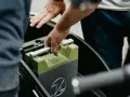 Mani che inseriscono una batteria verde in un vano. La durata della batteria della macchina è fondamentale per l'autonomia.