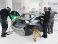 Operai saldano il telaio macchina in officina. Uno di loro usa una saldatrice, mentre gli altri osservano e lavorano sulla carrozzeria.