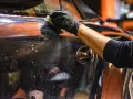 Mano guantata pulisce la carrozzeria lucida, sperando di non trovare vernice scheggiata da sassolino.