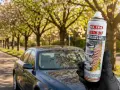 Mano guantata tiene spray MAFRA Resin Off per rimuovere resina e lucidare la plastica dell'auto, con auto scura sullo sfondo.