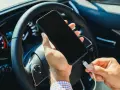 Mano che collega un cavo a uno smartphone, con il volante e il quadro strumenti dell'auto sullo sfondo. Se la batteria è scarica, il quadro si accende.