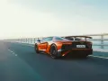 Arancia Lamborghini sfreccia su un ponte, i suoi cavalli scatenati sull'asfalto. L'auto sportiva domina la scena, un'icona di velocità.