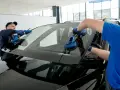 Tecnici installano un parabrezza, usando ventose. Il tempo asciugatura colla parabrezza è cruciale per la sicurezza.
