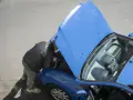 Uomo con giacca in pelle controlla la **macchina ferma** con il cofano aperto, forse un problema alla **batteria**.
