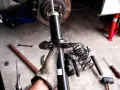 Gloved hand holding a car shock absorber with tools and springs on the ground.