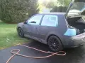 Auto grigia con nastro blu sui finestrini, pronta per la vernice per auto a rullo. Tubo da giardino sul vialetto.