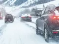 Auto con trazione posteriore sulla neve, luci accese, in un paesaggio montano innevato.