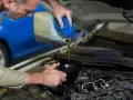 Meccanico versa olio motore da una tanica in un imbuto, risolvendo una perdita olio motore lato destro.