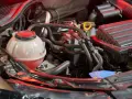 Serbatoio trasparente con liquido rosso, parte dell'impianto di raffreddamento del motore, circondato da tubi e componenti meccanici.
