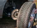 Mani che montano una gomma nuova su un cerchio, con il mozzo dell'auto visibile. La rotazione gomme auto è fondamentale per l'usura uniforme.