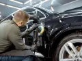 Dettaglio di un professionista che lucida una carrozzeria metallizzata nera per eliminare graffi, con lucidatrice rotativa.