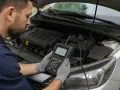 Meccanico con guanti grigi controlla con uno scanner diagnostico perché la centralina auto non parte.