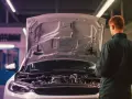 Meccanico esamina il motore turbo aspirato di un'auto con il cofano aperto in officina.