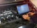 Meccanico controlla il motore di un'auto con un laptop, analizzando dati per ottimizzare l'anticipo automatico motori diesel.