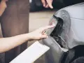 Due mani esaminano i danni alla carrozzeria auto, una indica il faro rotto, l'altra tiene una cartella per la perizia.