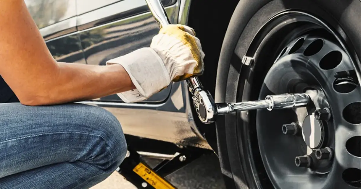 Persona con guanti gialli effettua il serraggio bulloni in kg con una chiave a bussola su una ruota d'auto sollevata da un cric.
