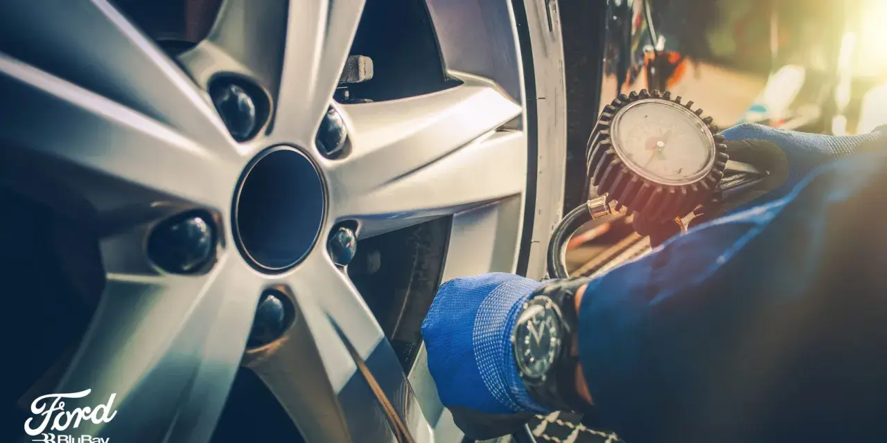 Controllo pneumatici con manometro su cerchio Ford. Guanto blu e orologio da polso.