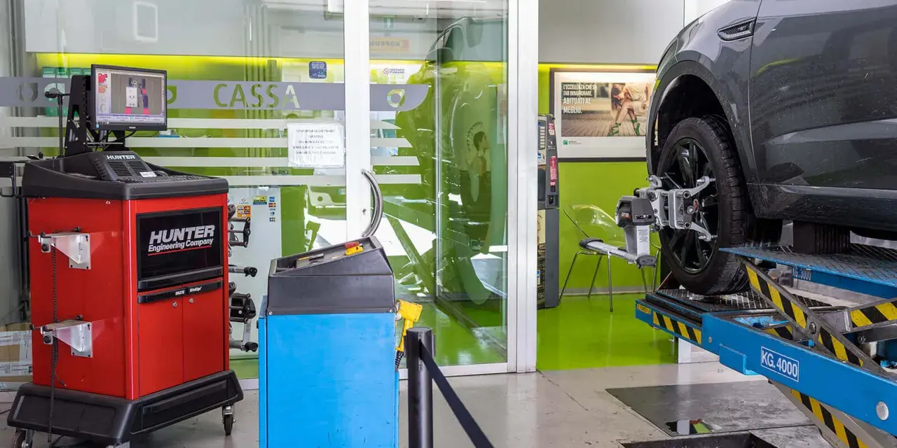Attrezzatura per la convergenza gomme in officina. Un'auto è sollevata su un ponte, con sensori applicati alla ruota.