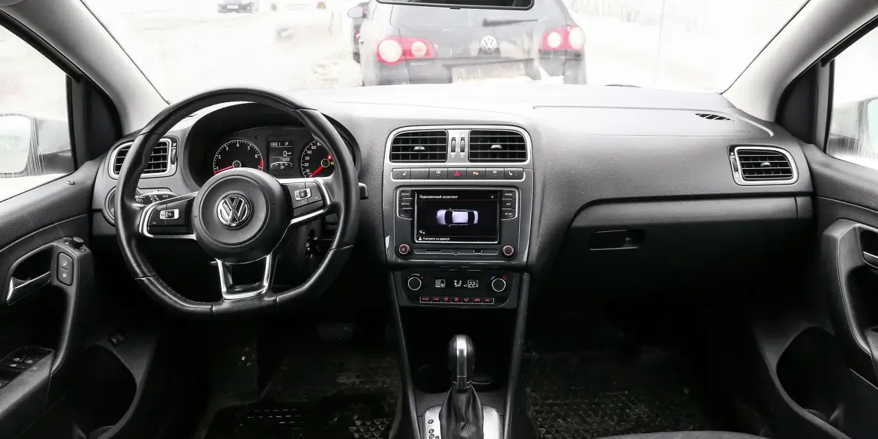 Interno di una Volkswagen Polo, con volante, cruscotto e cambio. Il display mostra il parcheggio assistito, utile per chi cerca il codice colore auto Volkswagen Polo.