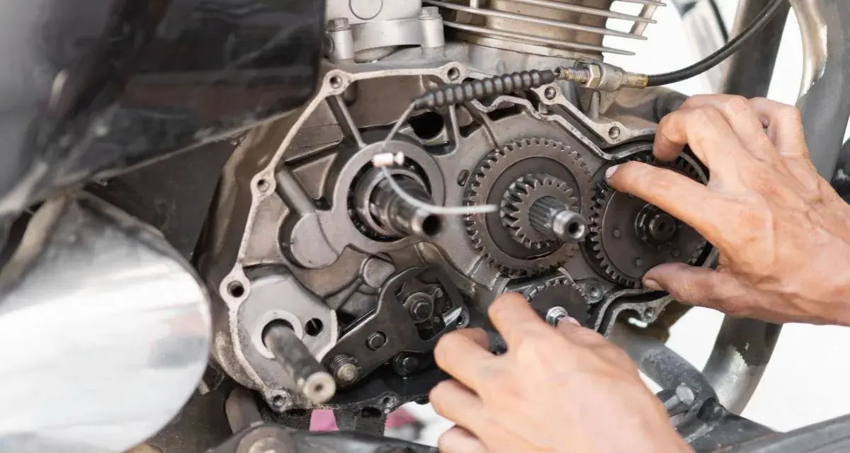 Mani che lavorano sul cambio di una moto, forse per risolvere una perdita di potenza auto benzina. Ingranaggi e meccanismi a vista.