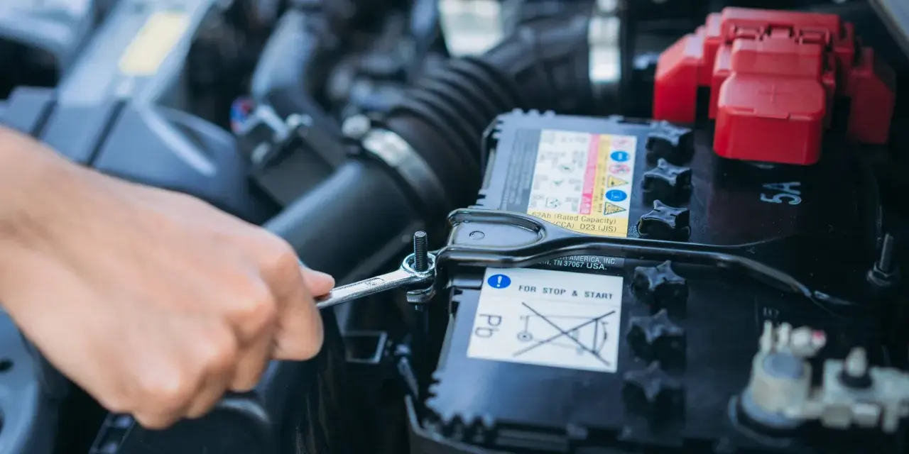 Mano con chiave inglese che lavora sulla batteria dell'auto. La batteria si scarica a vettura ferma, un problema comune per le auto con sistema Start & Stop.