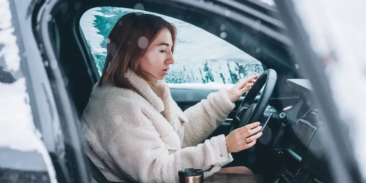 Donna al volante in un'auto coperta di neve, con le mani sul volante. Impara come guidare sulla neve in sicurezza.