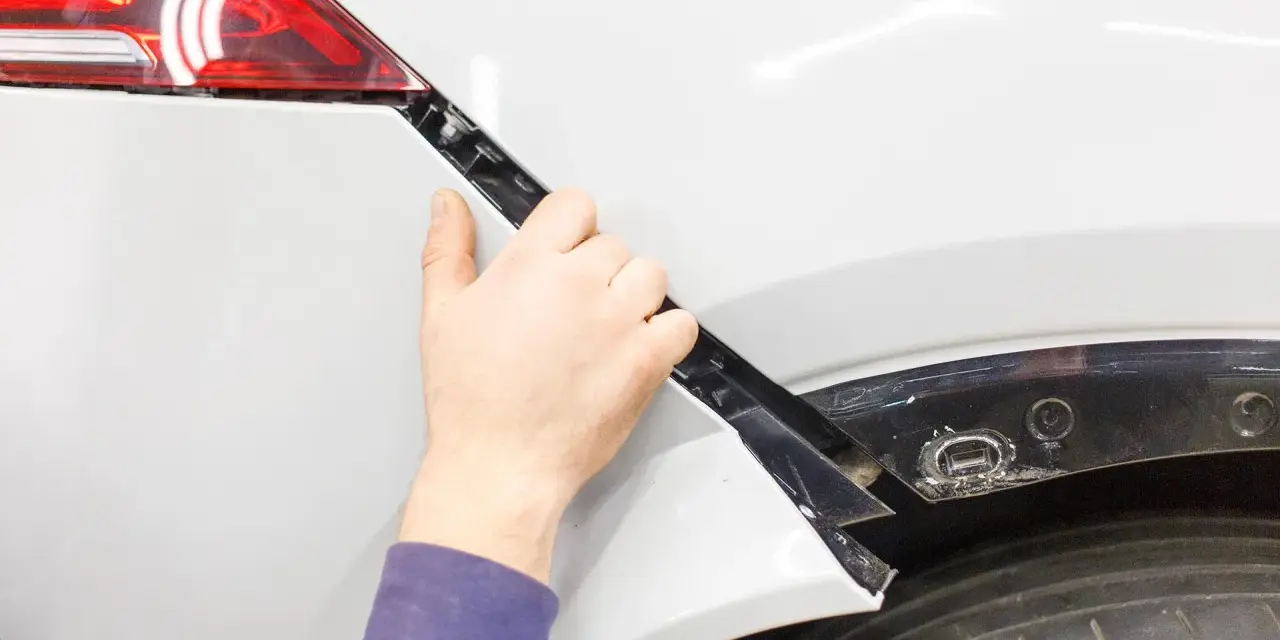 Mano che lavora alla riparazione paraurti in plastica di un'auto bianca.
