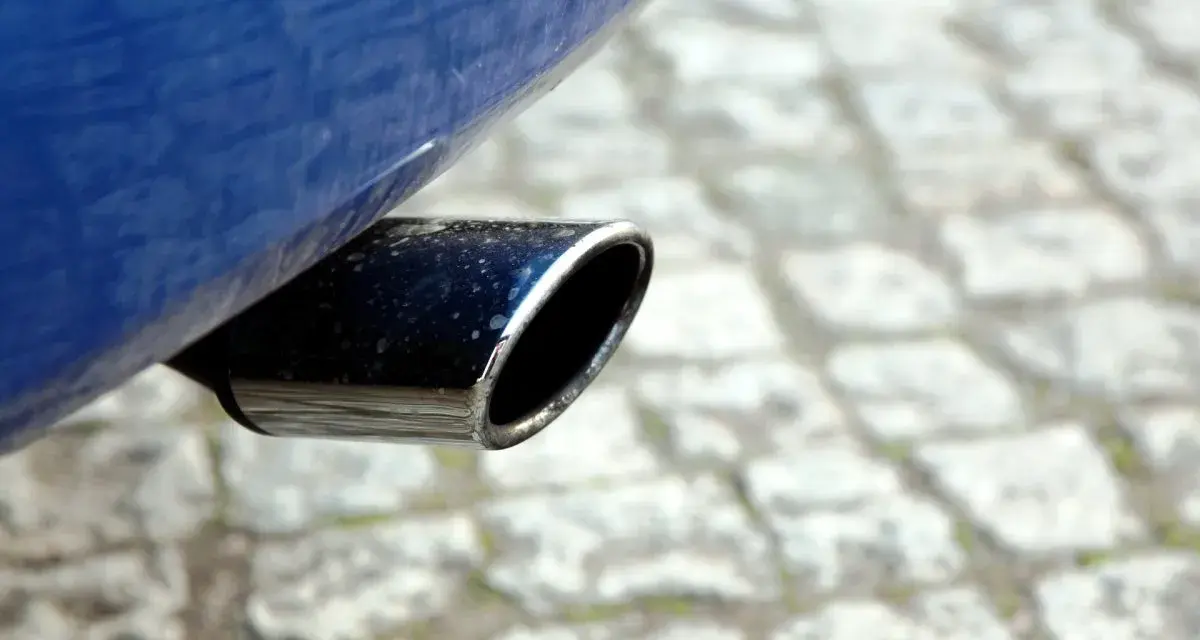 Il tubo di scarico cromato di un'auto blu, parte del silenziatore che attutisce il rumore del motore, su un selciato.