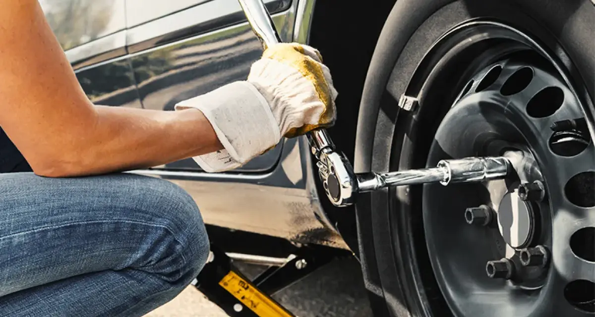 Persona con guanti gialli usa una chiave per serrare i bulloni della ruota di un'auto sollevata da un cric. Il significato di "nm" è la coppia di serraggio.