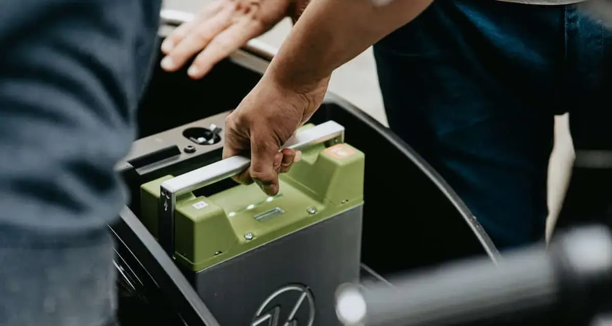 Mani che inseriscono una batteria verde in un vano. La durata della batteria della macchina è fondamentale per l'autonomia.