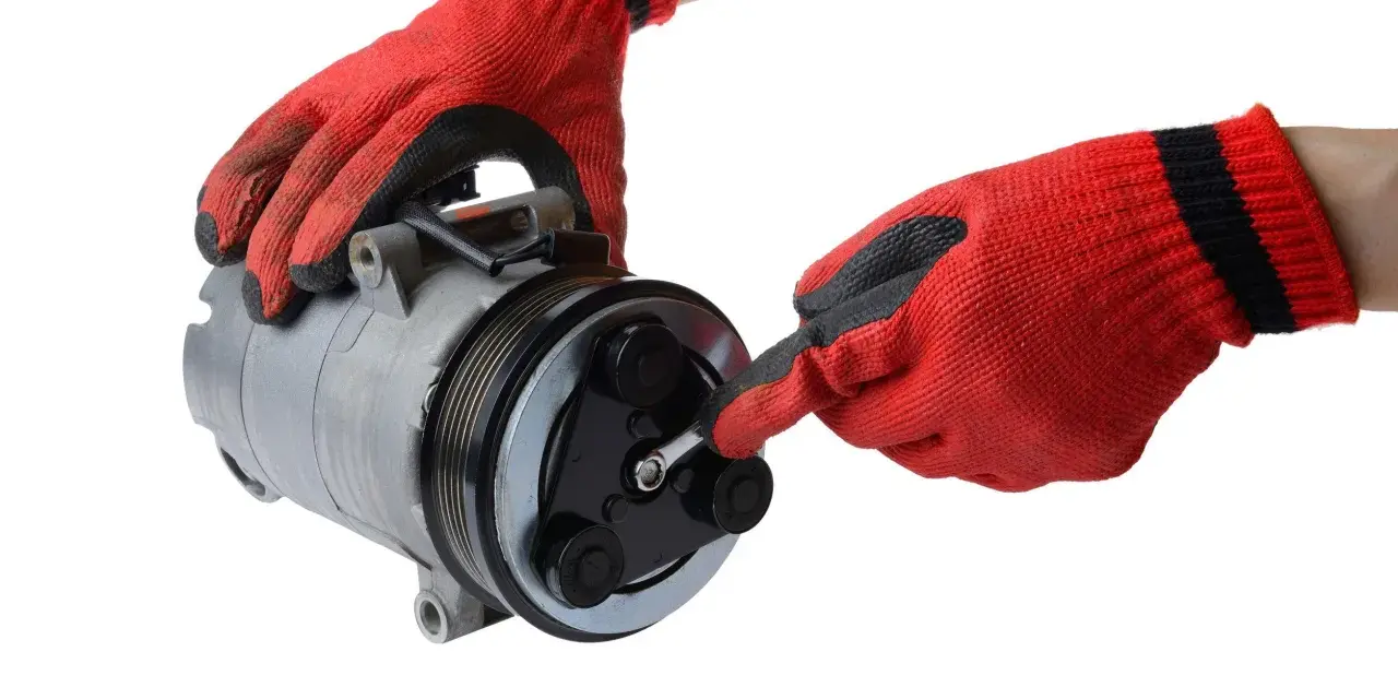Mani guantate rosse lavorano su un compressore per la sostituzione del compressore aria condizionata auto.