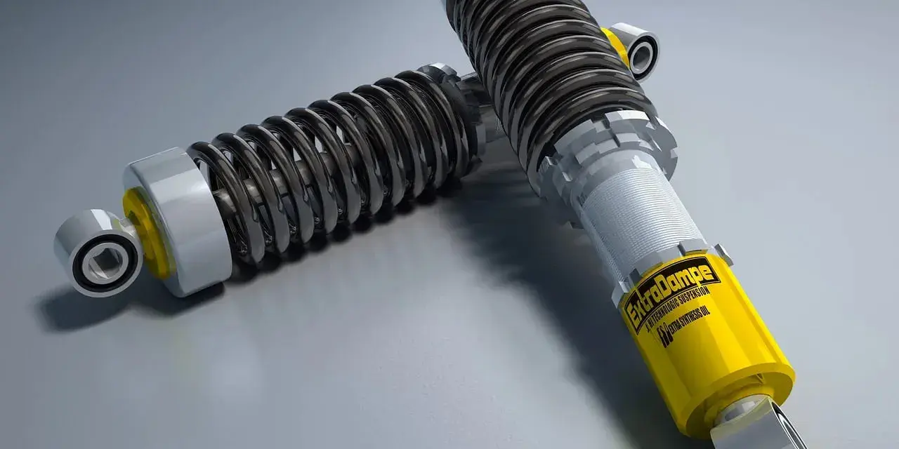 Due ammortizzatori auto di alta qualità, uno giallo con logo "ExtraDampe", pronti a migliorare le prestazioni su strada.
