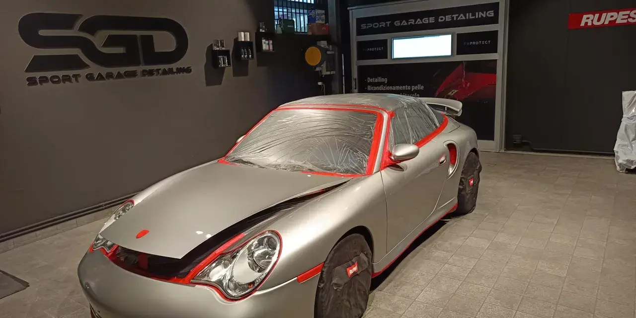 Auto sportiva pronta per la verniciatura, con protezioni rosse e cellophane. Il logo "SGD Sport Garage Detailing" è visibile.