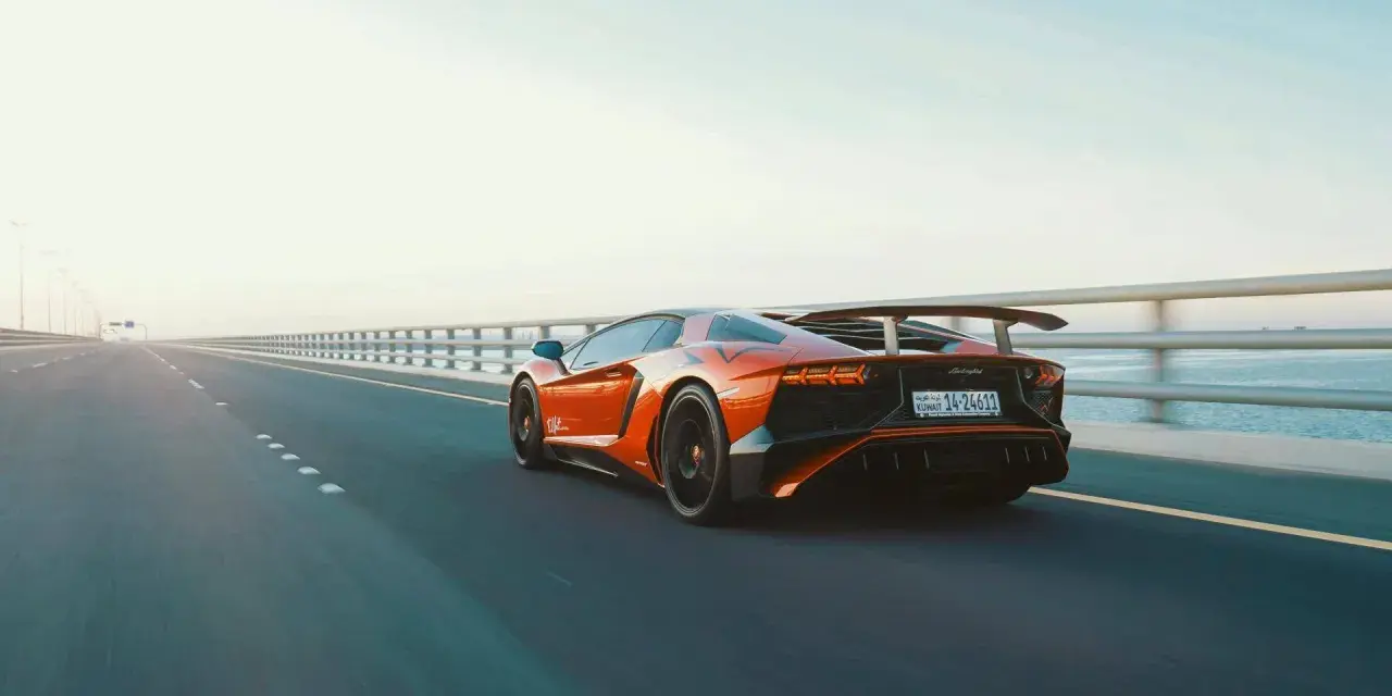 Arancia Lamborghini sfreccia su un ponte, i suoi cavalli scatenati sull'asfalto. L'auto sportiva domina la scena, un'icona di velocità.