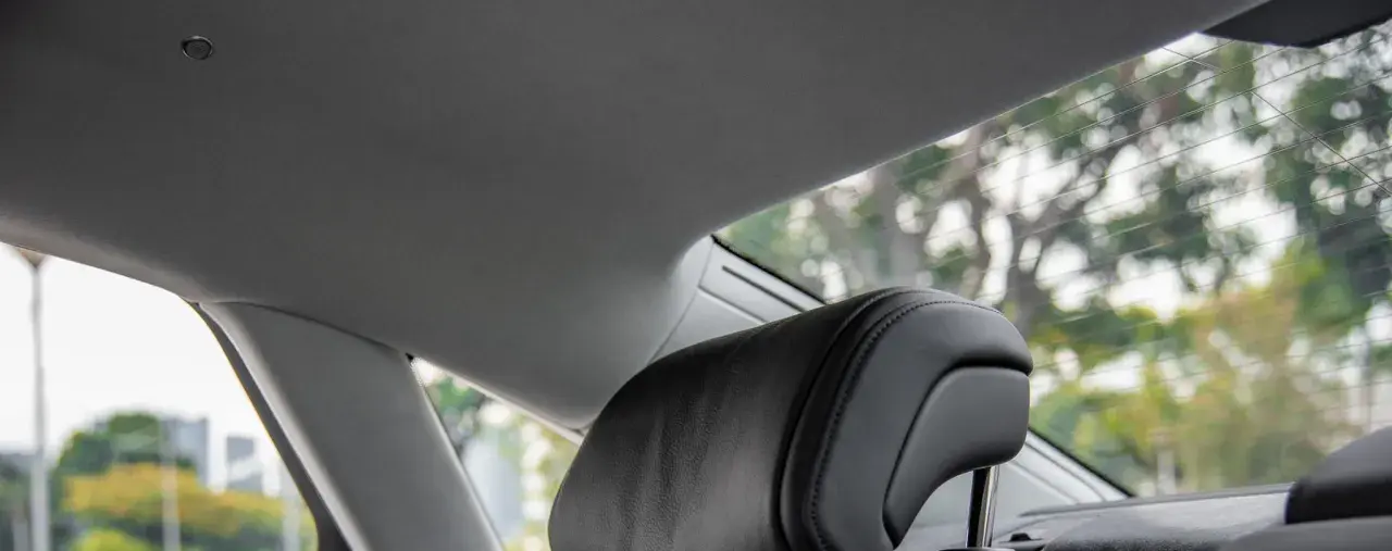 Interno auto con tettuccio grigio e poggiatesta in pelle nera. Si vede il lunotto con alberi sfocati all'esterno, come se si potesse incollare il cielo dell'auto senza smontarlo.