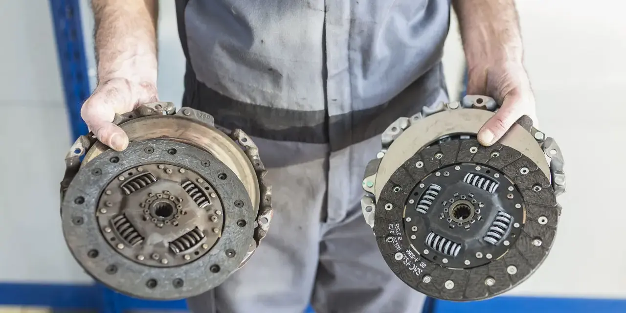 Meccanico mostra due dischi frizione, essenziali per capire a cosa serve la frizione: disconnettere il motore dalla trasmissione per cambiare marcia.