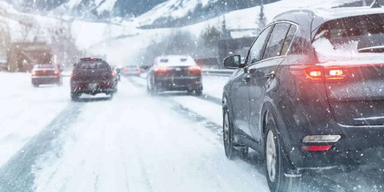 Auto con trazione posteriore sulla neve, luci accese, in un paesaggio montano innevato.