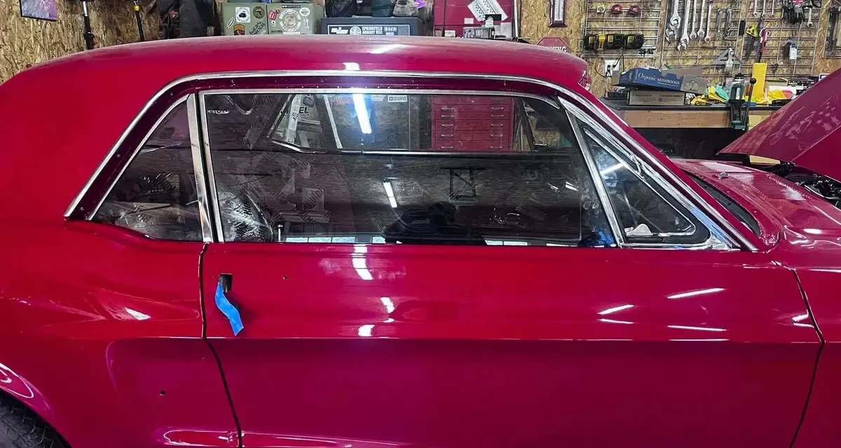 Auto d'epoca con vernice rosso candy apple lucida, in un garage con attrezzi appesi.