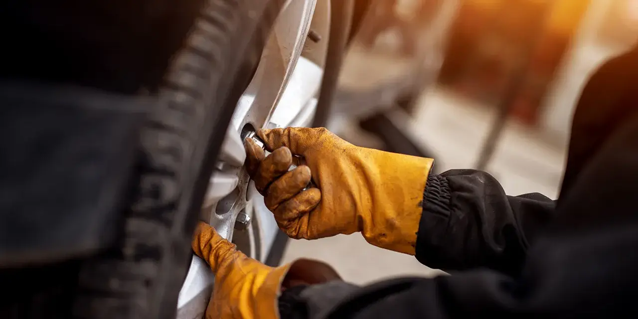 Mani guantate stringono bulloni ruota auto, seguendo la tabella coppia serraggio per sicurezza.
