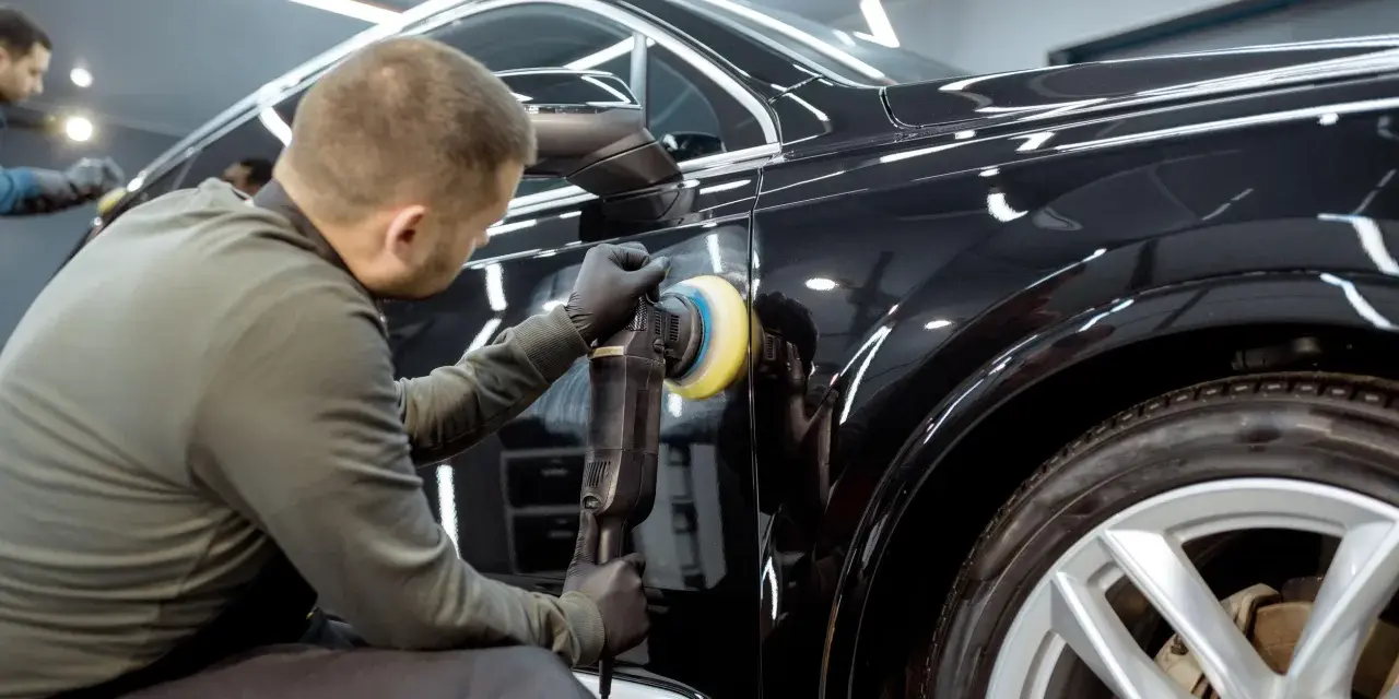 Dettaglio di un professionista che lucida una carrozzeria metallizzata nera per eliminare graffi, con lucidatrice rotativa.