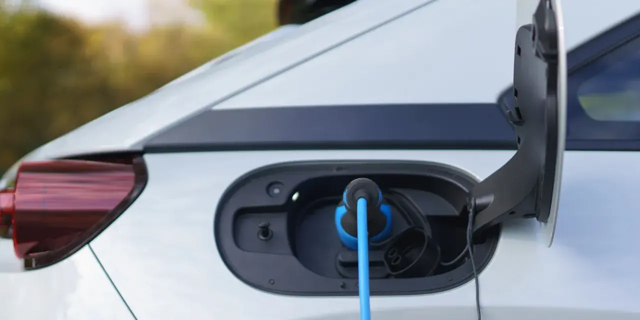 Auto elettrica in carica, con cavo blu collegato alla porta. La coppia motore è pronta per la prossima avventura.